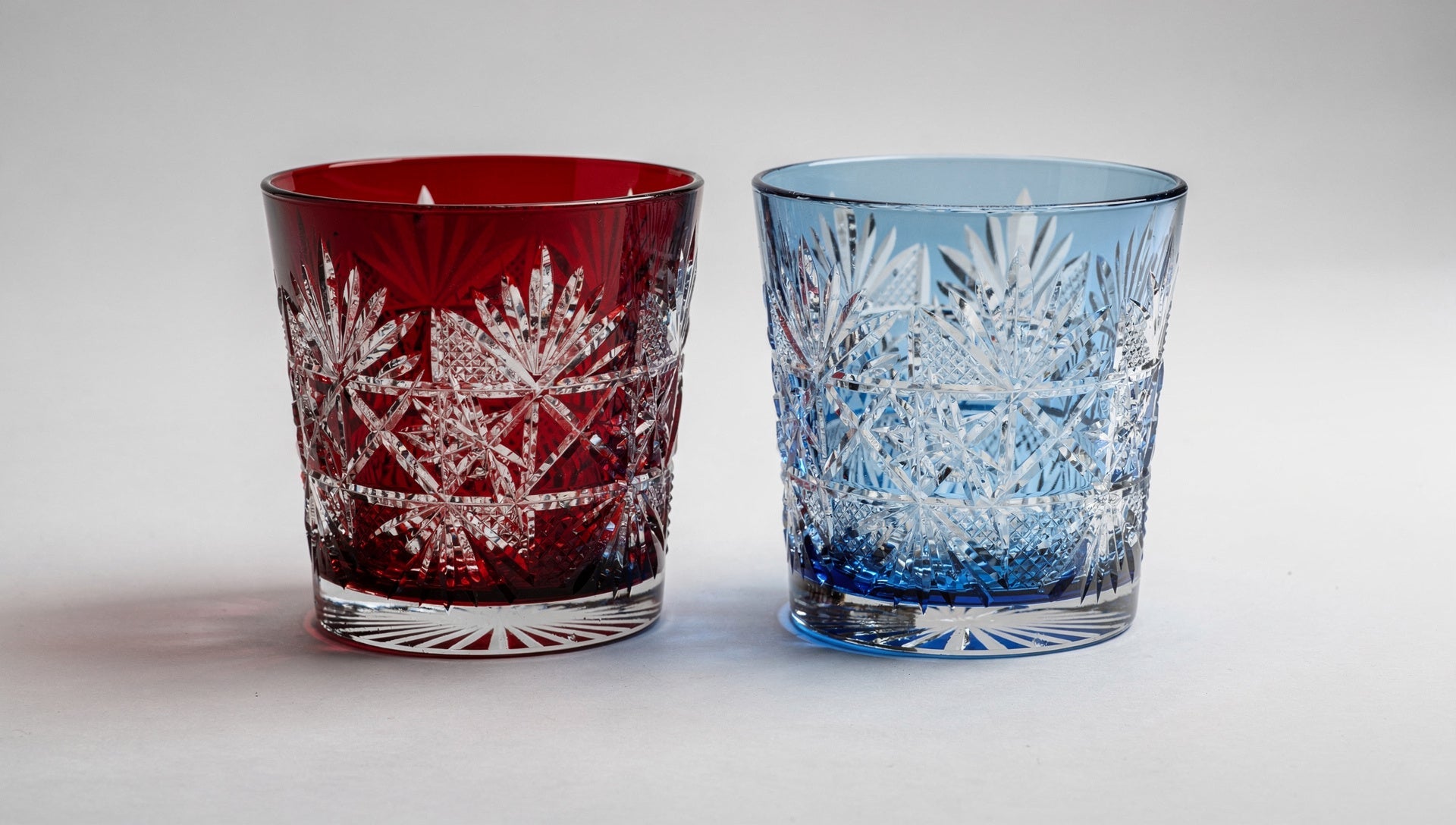 A ruby overlay cut glass beside a cooler cobalt overlay glass on pale grey.