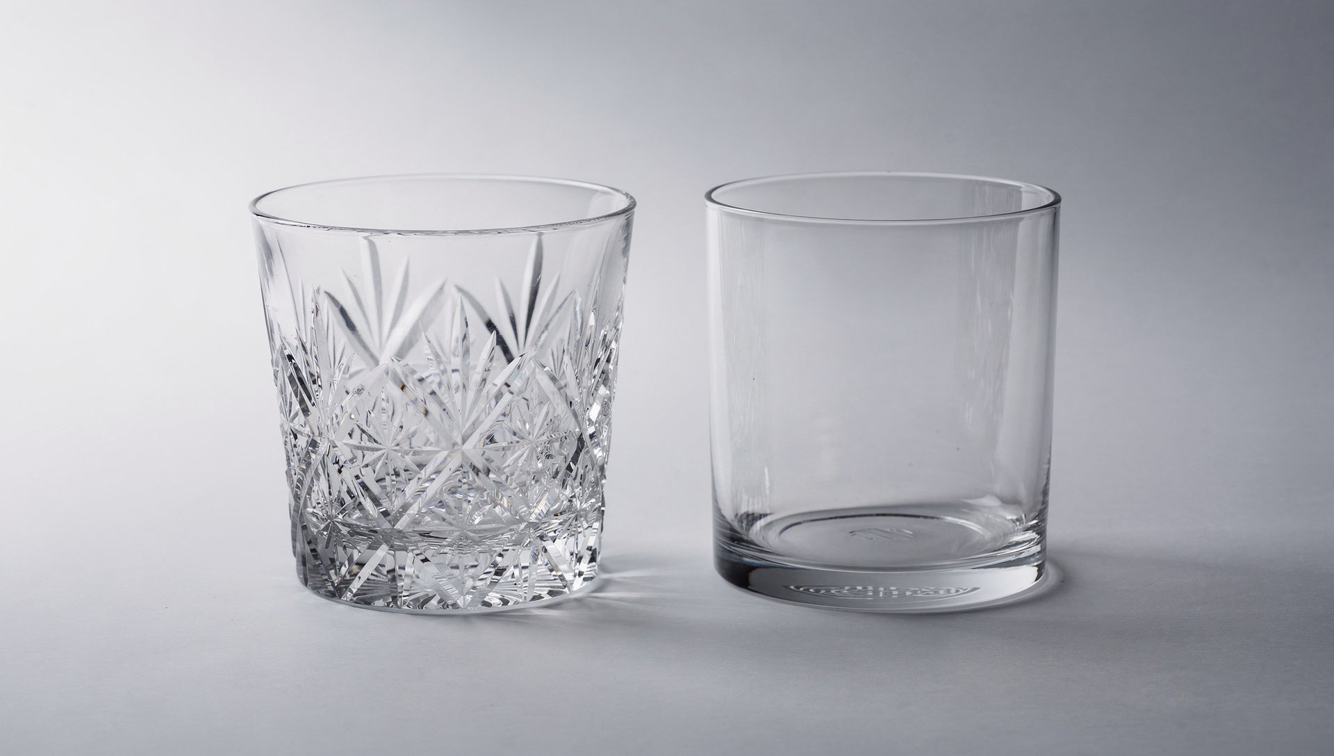 One cut glass beside a smooth uncut glass blank on pale grey.
