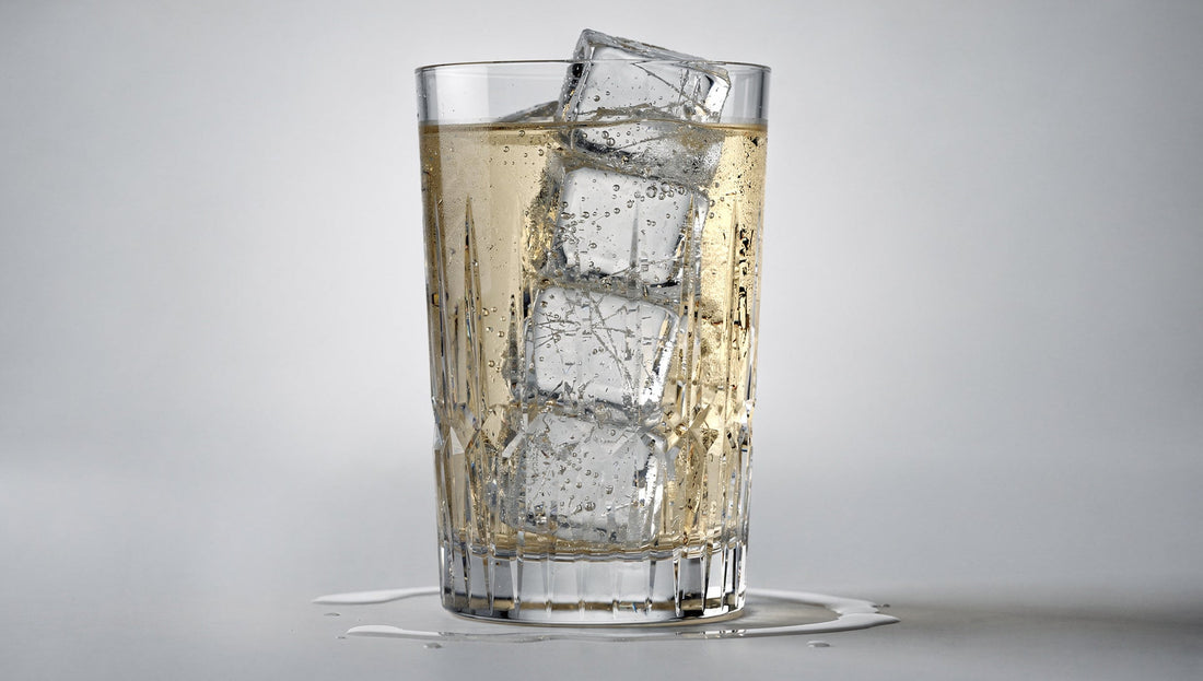A tall highball with clear ice and a pale whisky-soda on pale grey.