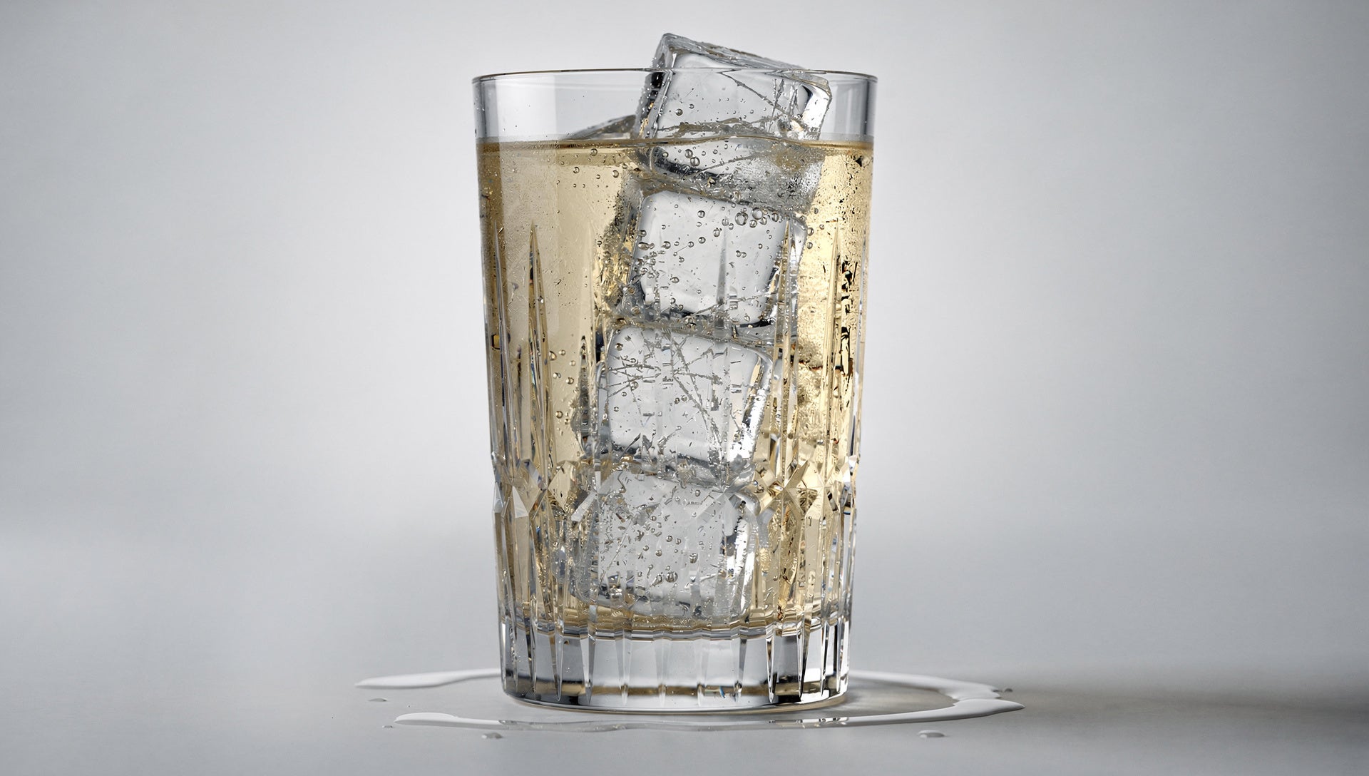 A tall highball with clear ice and a pale whisky-soda on pale grey.