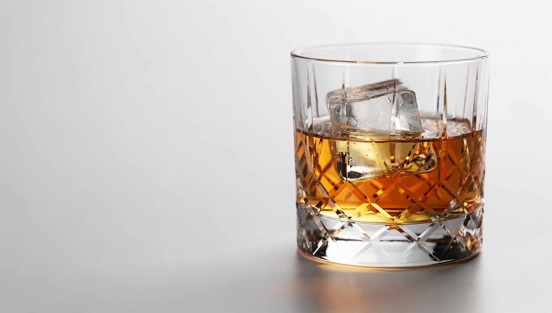 A Japanese cut-glass rocks glass with one large clear ice cube seated cleanly, pale ground and cold light.