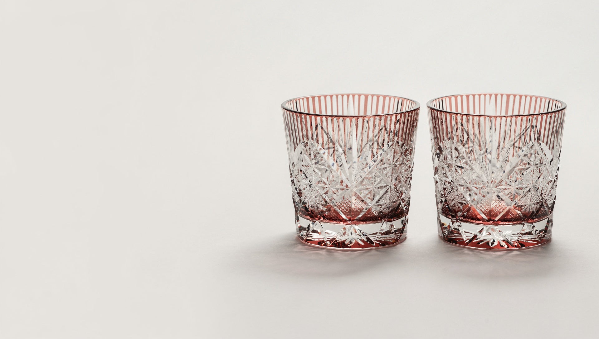 A quiet pair of empty Japanese cut-glass rocks glasses standing together on a pale ground, no ribbon.