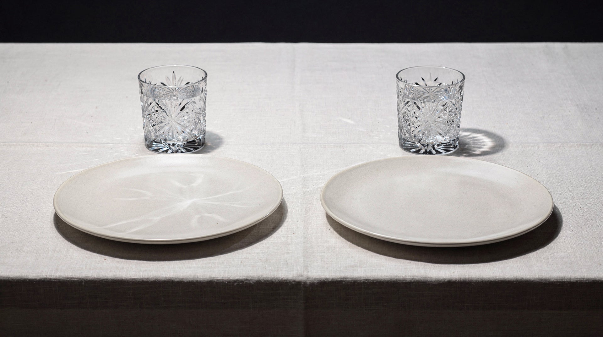 Two quiet place settings, each with one Japanese cut glass and a plain plate