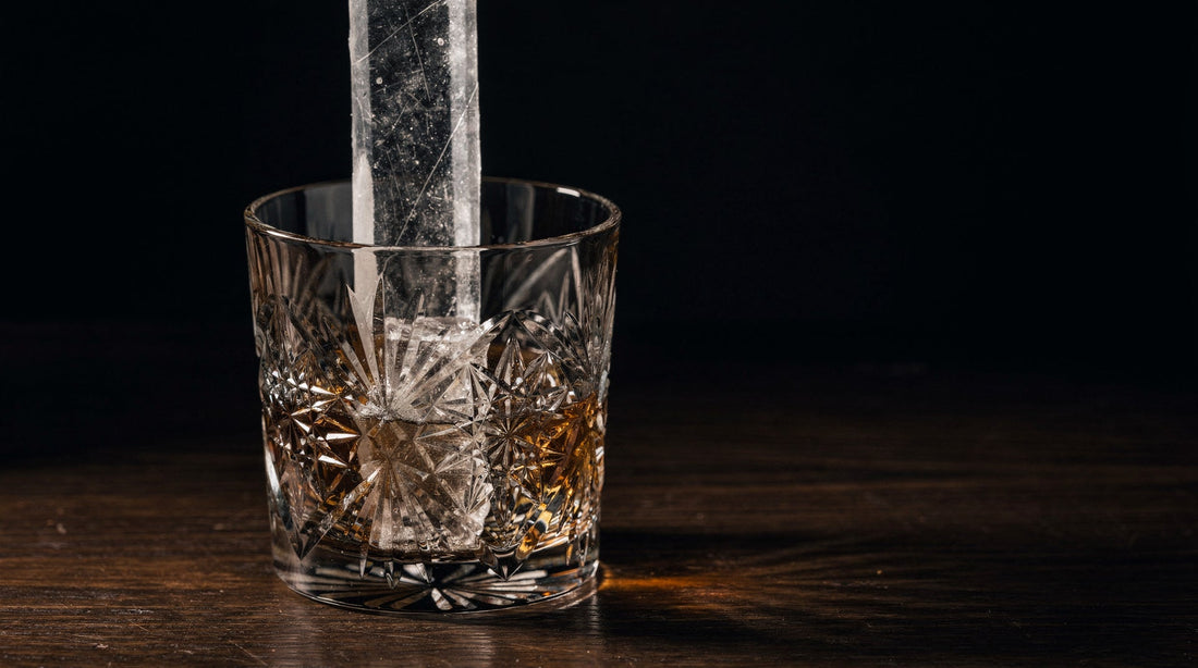 A dim bar top with one cut rocks glass and a tall column of clear ice