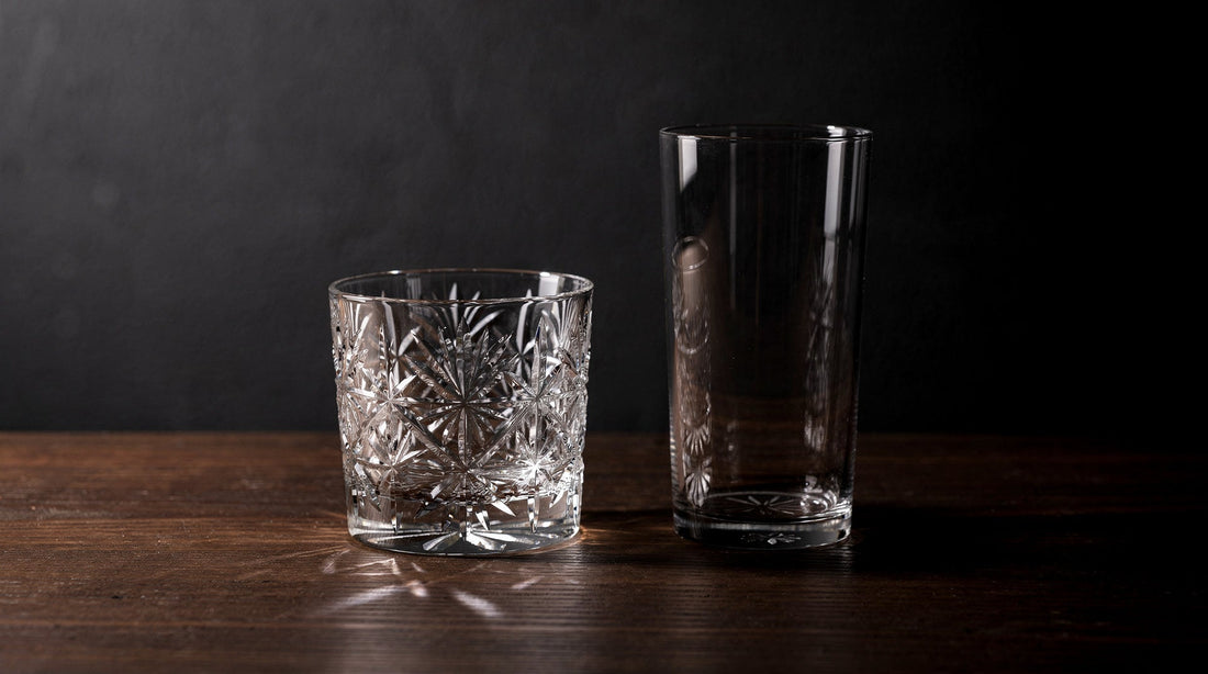 A short Japanese cut glass beside a taller plain tumbler on dark wood