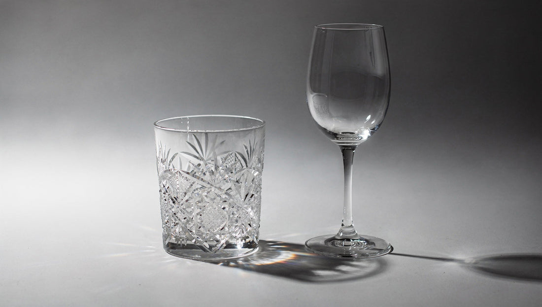 A faceted Japanese cut-glass rocks tumbler beside a typical stemmed crystal wine glass on a pale ground.