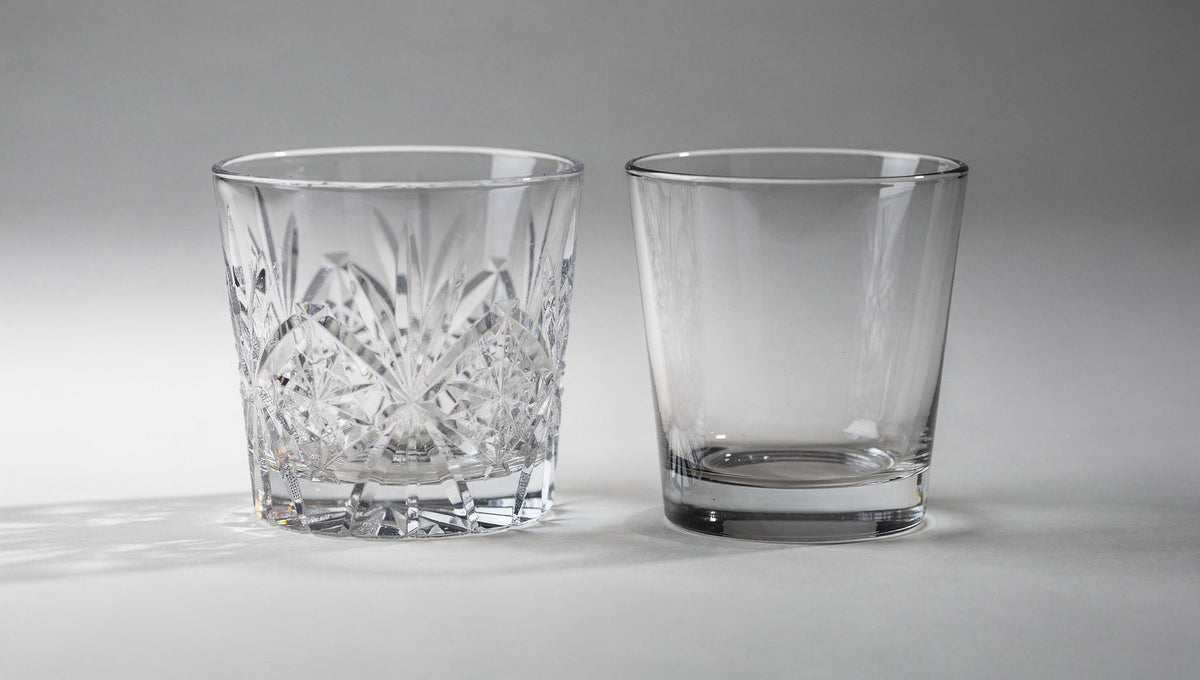 Un verre japonais à taille nette à côté d'un tumbler en verre pressé, moins cher et aux formes arrondies, sur fond pâle.