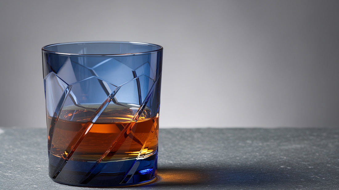 A cobalt Japanese cut rocks glass with a short amber pour on cool grey slate, soft rim light on the facets and base