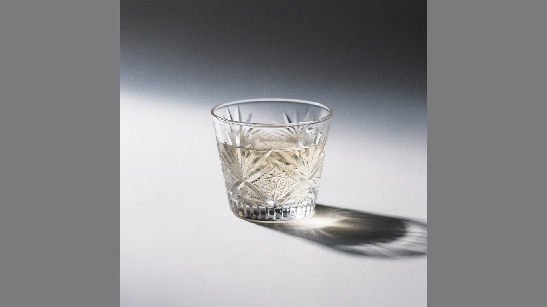 A small clear Japanese cut-glass sake cup with a small pour on a pale ground
