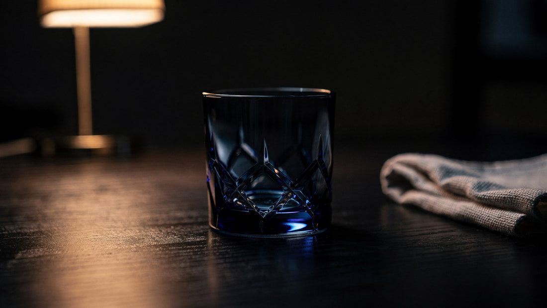 An empty dry cobalt Japanese cut rocks glass on a dark table under a low lamp, with a folded linen cloth beside it