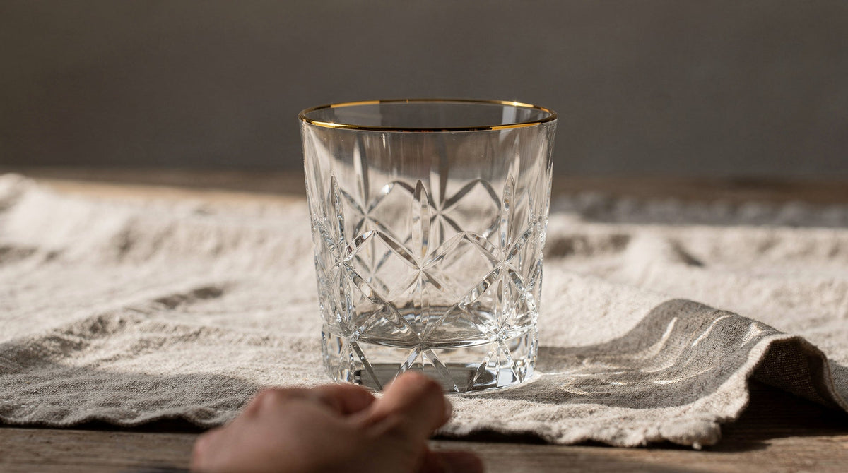 Clear Japanese cut rocks glass on linen, a hand resting at the base