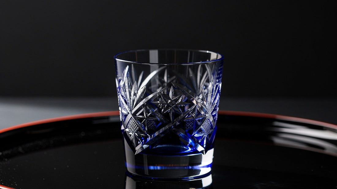 A cobalt Japanese cut rocks glass on a black lacquer tray with hard side light on the facets