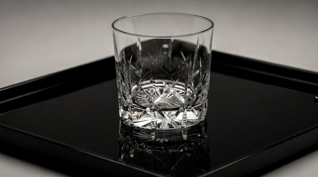 An empty clear Japanese cut rocks glass on a black lacquer tray, base readable, quiet specular light.