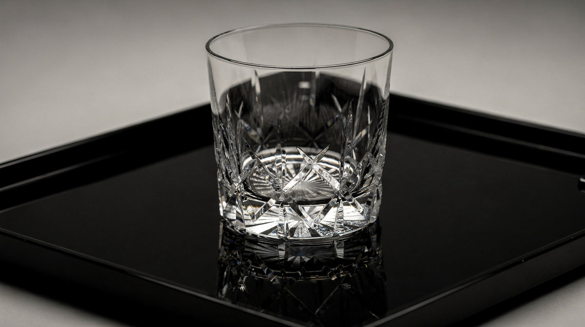 An empty clear Japanese cut rocks glass on a black lacquer tray, base readable, quiet specular light.