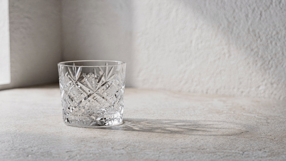 A clear Japanese cut rocks glass empty and dry on a pale plaster plane under soft window side-light