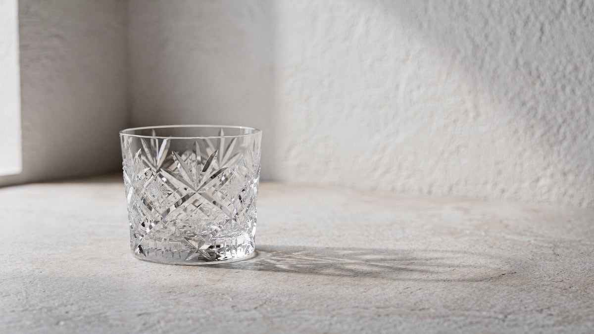 A clear Japanese cut rocks glass empty and dry on a pale plaster plane under soft window side-light