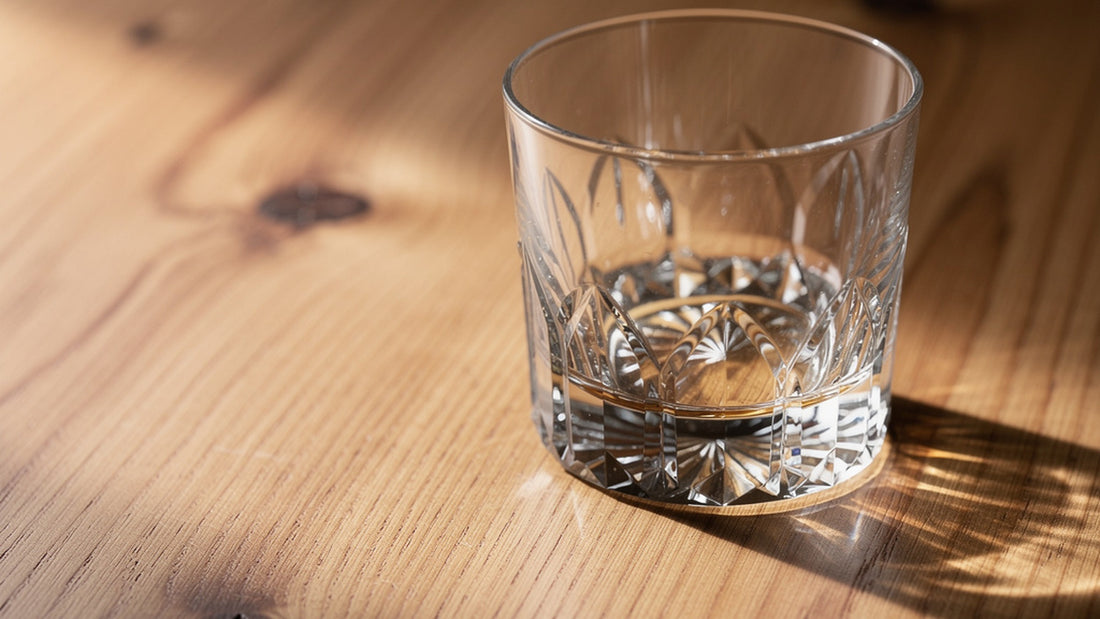 A clear Japanese cut rocks glass standing upright on warm cedar under soft side light