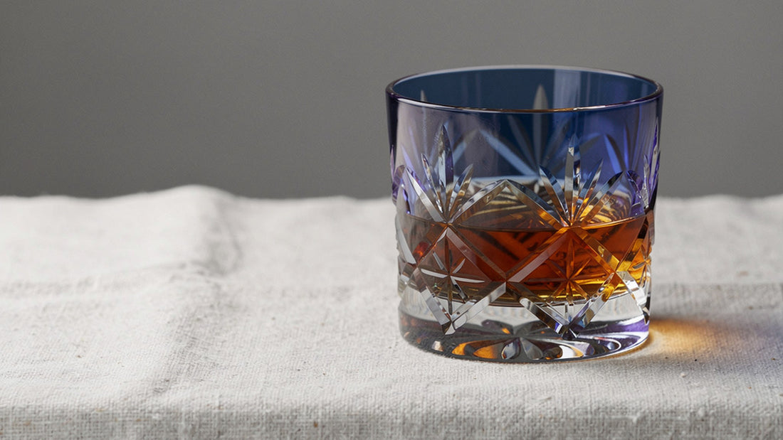 A cobalt Japanese cut rocks glass with a short amber pour on pale linen under soft side window light