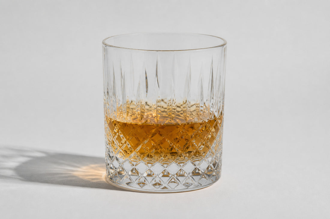 A clear Japanese cut rocks glass on pale ground with a short amber pour, three-quarter view