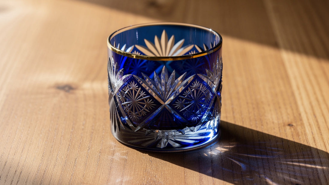 A cobalt Japanese cut rocks glass alone on warm cedar with side light along the rim and facets