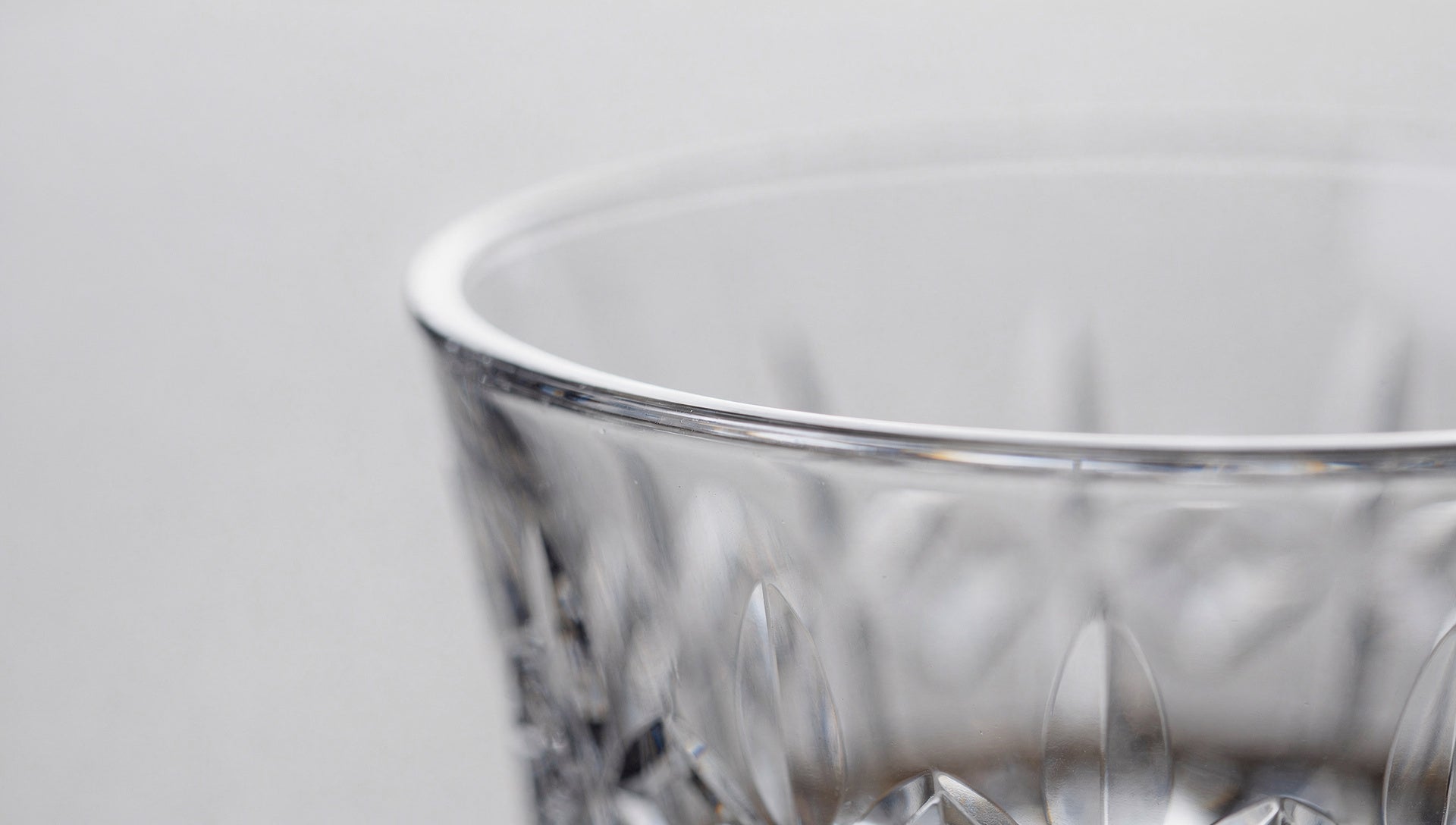 Extreme close-up of a thin clear Japanese cut-glass rim against a pale field, one highlight running the circle.
